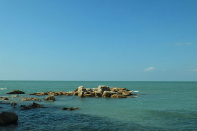 Rocks on sea against clear blue sky