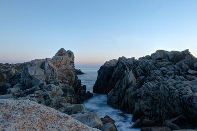 Rocks by sea against clear sky