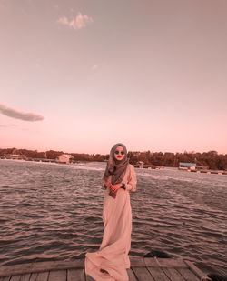 Portrait of young woman standing against sky during sunset