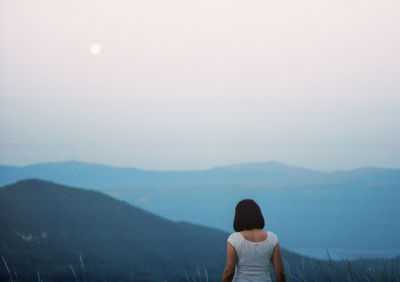 Rear view of woman standing on mountain against sky