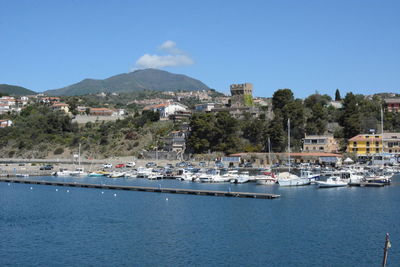 Boats moored at harbor by town against clear blue sky