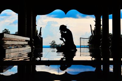 Silhouette man standing by swimming pool against sky