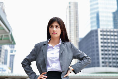 Portrait of young woman standing against buildings in city