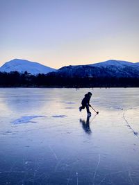 Boy playing ice hockey on frozen lake