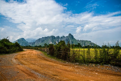 Scenic view of dirt road with field and mountain against sky