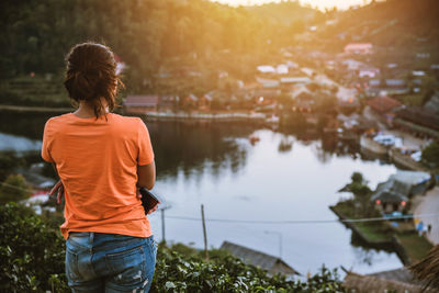 Rear view of woman standing by plants over lake during sunset