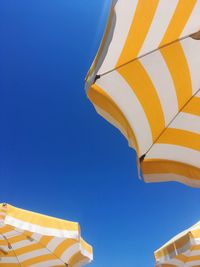 Low angle view of yellow umbrella against clear blue sky