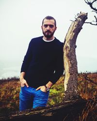 Portrait of young man standing on tree trunk