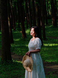 Woman standing by tree trunk in forest