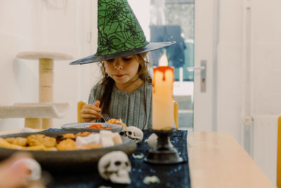 A girl in a green witch hat eats halloween food.