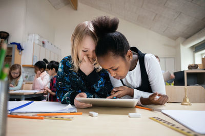 Multi-ethnic students using digital tablet at desk in classroom