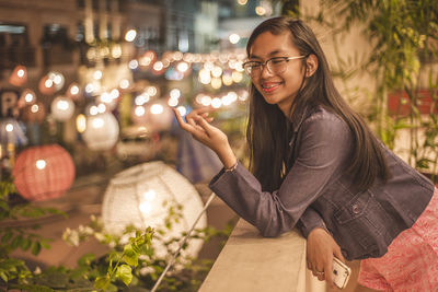 Portrait of smiling young woman in city at night