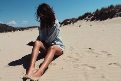 Sensuous young woman sitting at beach against sky