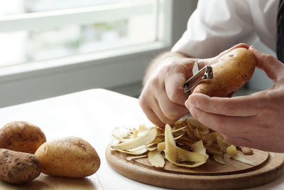 Cropped image of chef peeling potatoes on table