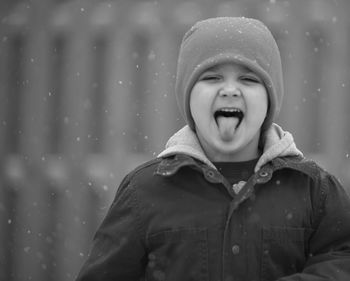 Portrait of cute boy sticking out tongue during snowfall