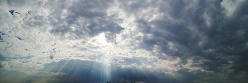 Low angle view of sunlight streaming through clouds