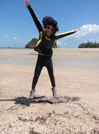 Portrait of happy girl with arms raised jumping at beach against sky