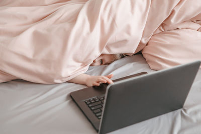 Shy scared girl lying in bed under blanket and learning in virtual online school class. kid working 