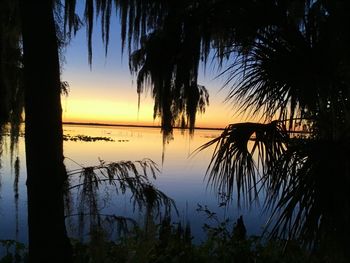 Silhouette trees by lake against sky during sunset