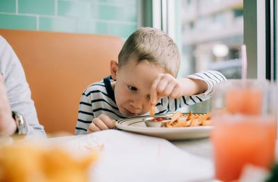 Young boy eating fries dipping them in sauce in a restaurant