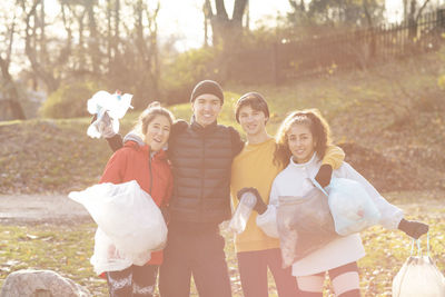 Smiling male and female environmentalists with microplastics garbage standing in park