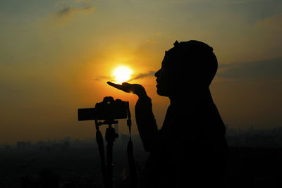 Silhouette woman photographing against sky during sunset
