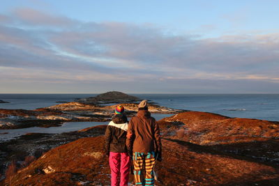 Rear view of man standing on rock by sea against sky