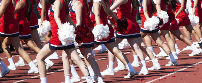 High school cheerleader's holding white pom poms are cheering on sidelines during a football game.