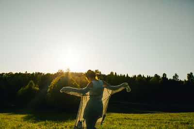 Rear view of a woman dancing on a field in sunlight.