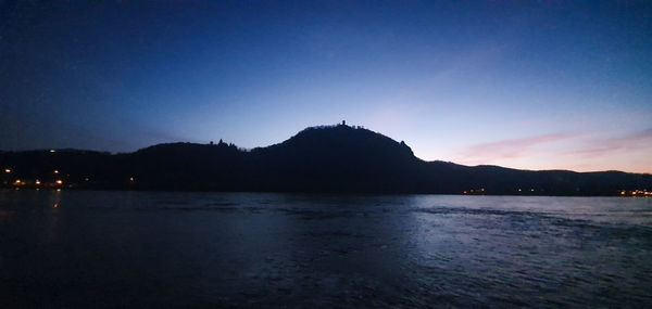 Scenic view of lake by silhouette mountains against clear sky