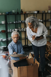 Senior salesman examining plate sitting by female colleague in antique shop