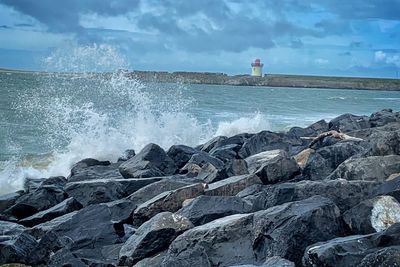 Waves splashing on rocks at shore against sky