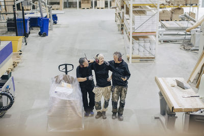 High angle view of smiling workers talking while standing by pallet jack in industry