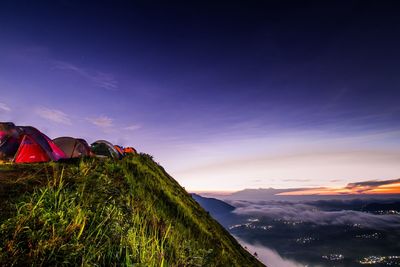 Tents on grassy hill against blue sky at dusk