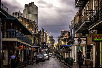 City street amidst buildings in city against cloudy sky