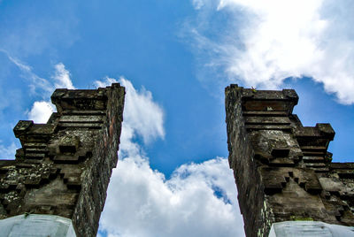 Low angle view of columns against cloudy sky at tanah lot on sunny day