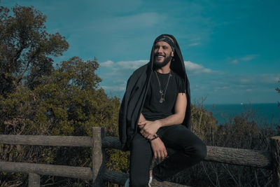 Portrait of smiling young man sitting against sky