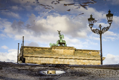 Low angle view of street light and brandenburg gate against cloudy sky