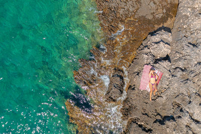 Aerial view of a girl sunbathing on the rocky beach,  adriatic sea in croatia