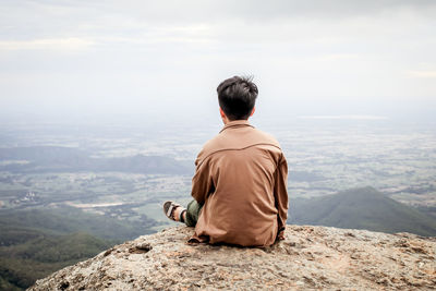 Rear view of woman sitting on mountain against sky