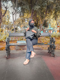 Full length of woman wearing mask looking away while sitting outdoors