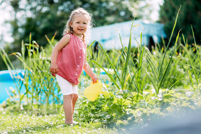 A little smiling girl is watering a strawberry bush in the garden from a children's toy