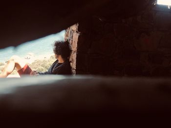 Young man seen through hole looking away while sitting against brick wall