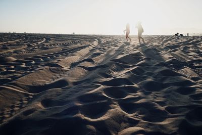 People walking on sand at beach against clear sky