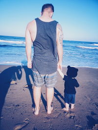 Rear view of father with baby standing on shore at beach