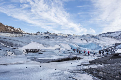 People hiking on snowcapped mountain against cloudy sky