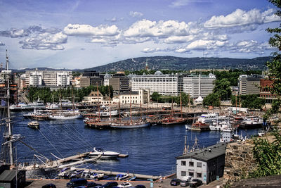 Sailboats moored in harbor by city against sky