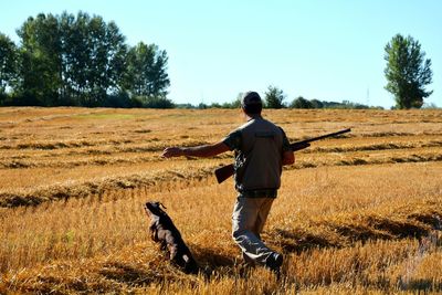 Rear view of man holding gun by dog on farm