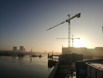 Silhouette cranes at harbor against sky during sunset