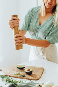 Young woman using manual pepper grinder to seasoning avocado